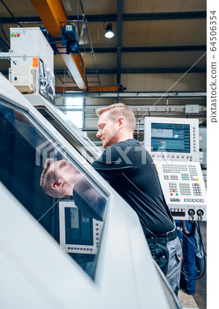 Worker resetting a cnc lathe machine in manufacturing factory Worker resetting a cnc lathe machine in manufacturing factory 64506354