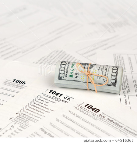 Tax forms lies near roll of hundred dollar bills. Tax forms lies near roll of hundred dollar bills. 64516365