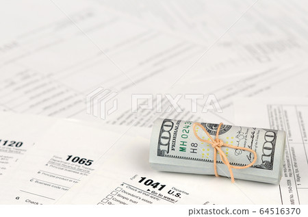 Tax forms lies near roll of hundred dollar bills. 64516370
