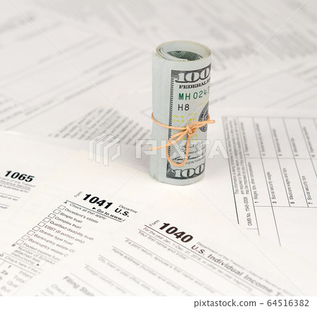 Tax forms lies near roll of hundred dollar bills. Tax forms lies near roll of hundred dollar bills. 64516382