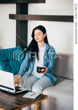 Woman working on laptop at home, enjoying coffee Woman working on laptop at home, enjoying coffee 64517875