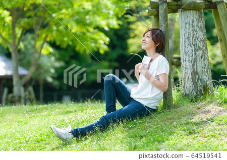 Woman looking up at the sky while reading a book in the shade of a tree 64519541