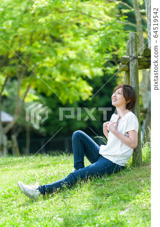 在樹蔭下看書的同時抬頭望著天空的女人 64519542