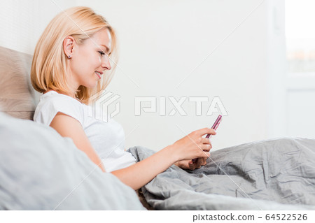 Beautiful young woman using phone in bed Beautiful young woman using phone in bed 64522526