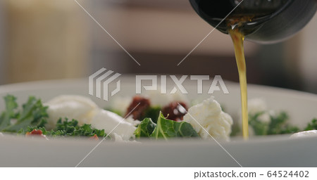 pour dressing to kale salad with sundried tomatoes and mozzarella in white bowl closeup pour dressing to kale salad with sundried tomatoes and mozzarella in white bowl closeup 64524402