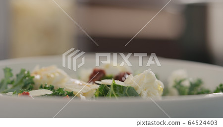 almond flakes falling on kale salad with sundried tomatoes and mozzarella in white bowl closeup 64524403