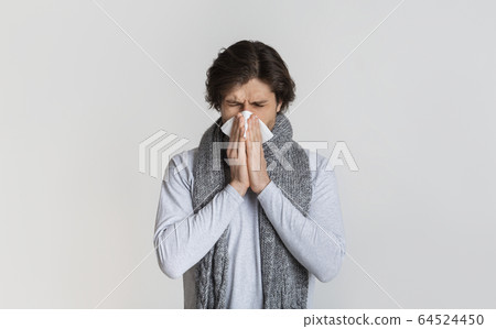 Man with scarf, blows nose in napkin 64524450