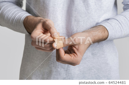 Man wrapping wound on finger with band-aid 64524481