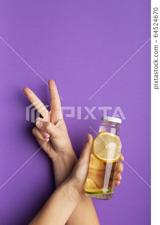 Female hand holding bottle with detox lemonade and showing v sign Female hand holding bottle with detox lemonade and showing v sign 64524670
