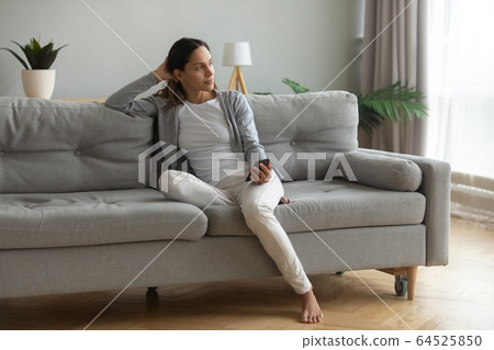 Beautiful woman sitting on couch, holding phone, waiting for call 64525850