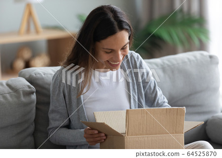 Smiling young woman unpacking parcel, opening cardboard box 64525870