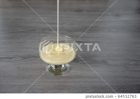 condensed milk in a transparent glass bowl on a wooden background condensed milk in a transparent glass bowl on a wooden background 64532763
