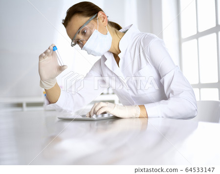 Female laboratory assistant analyzing a blood sample at hospital. Medicine, health care and researching concept Female laboratory assistant analyzing a blood sample at hospital. Medicine, health care and researching concept 64533147
