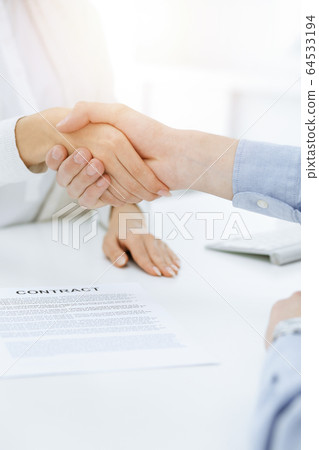 Casual dressed businessman and woman shaking hands after contract signing in sunny office. Handshake concept Casual dressed businessman and woman shaking hands after contract signing in sunny office. Handshake concept 64533194