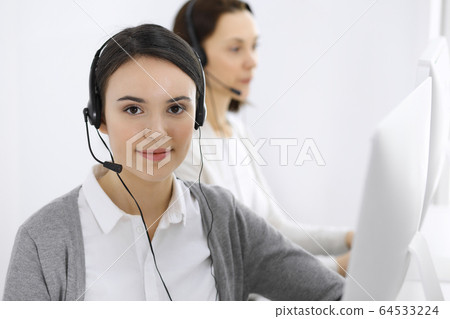 Call center. Casual dressed woman working in headset with diverse colleagues at office. Business concept Call center. Casual dressed woman working in headset with diverse colleagues at office. Business concept 64533224