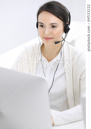 Call center. Casual dressed woman working in headset with diverse colleagues at office. Business concept Call center. Casual dressed woman working in headset with diverse colleagues at office. Business concept 64533232