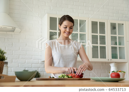 Smiling attractive woman chopping vegetables for cooking salad. 64533713