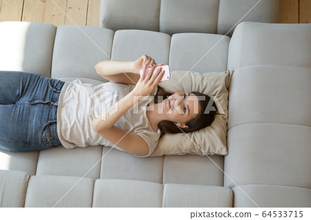 Smiling attractive young woman using smartphone lying on sofa. 64533715