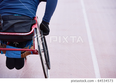Rear view of physically impaired athlete moving in racing wheelchair on track Rear view of physically impaired athlete moving in racing wheelchair on track 64534573