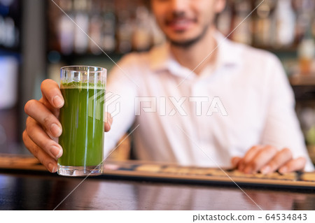 Hand of waiter putting glass of vegetable smoothie of green color on bar counter Hand of waiter putting glass of vegetable smoothie of green color on bar counter 64534843