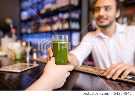 Hand of young woman taking glass of fresh salary or broccoli smoothie 64534845