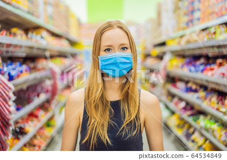 Alarmed female wears medical mask against coronavirus while grocery shopping in supermarket or Alarmed female wears medical mask against coronavirus while grocery shopping in supermarket or 64534849