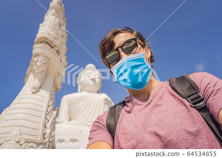 Man tourist in medical mask on background of Big Buddha statue Was built on a high hilltop of Phuket Man tourist in medical mask on background of Big Buddha statue Was built on a high hilltop of Phuket 64534855
