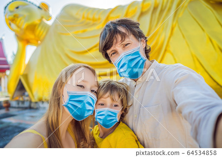 Happy tourists mother, father and son in medical mask on background ofLying Buddha statue Tourists Happy tourists mother, father and son in medical mask on background ofLying Buddha statue Tourists 64534858
