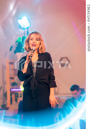 Pretty blond girl with evening makeup holding microphone by her mouth 64534961