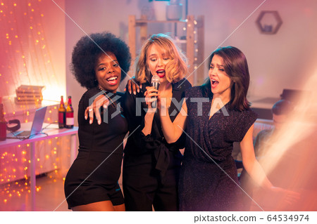 Group of young cheerful women in black dresses singing in front of camera 64534974