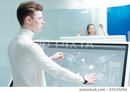 Young software engineer in smart goggles standing by large interactive display Young software engineer in smart goggles standing by large interactive display 64535094