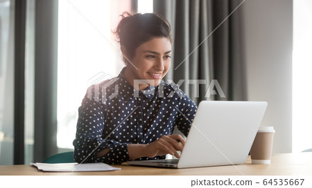 Happy young indian businesswoman using computer sit at office desk Happy young indian businesswoman using computer sit at office desk 64535667