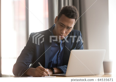 Serious african businessman ceo making notes working doing paperwork Serious african businessman ceo making notes working doing paperwork 64535671