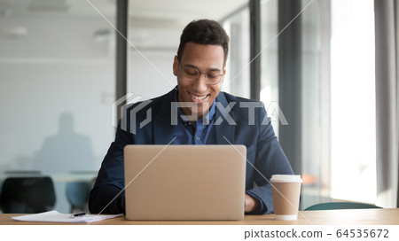 Happy african businessman working using laptop sit at office desk 64535672