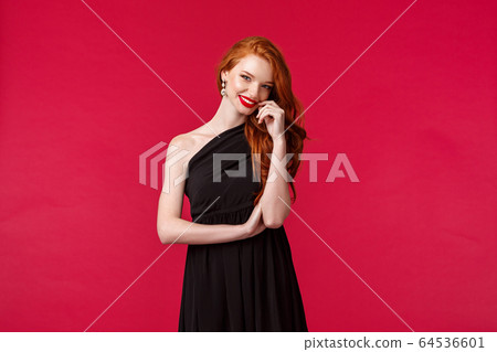 Elegance, fashion and woman concept. Portrait of seducative and sensual woman with ginger hair in elegant evening black dress, attend prom or party, wearing red lipstick, smiling coquettish Elegance, fashion and woman concept. Portrait of seducative and sensual woman with ginger hair in elegant evening black dress, attend prom or party, wearing red lipstick, smiling coquettish 64536601