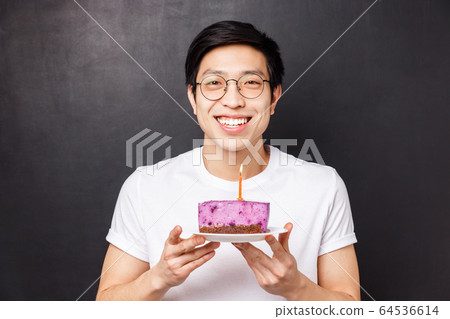Celebration, holiday and birthday concept. Close-up portrait of happy, cheerful b-day guy holding cake with lit candle, smiling upbeat, thinking what wish make and blow-out, black background Celebration, holiday and birthday concept. Close-up portrait of happy, cheerful b-day guy holding cake with lit candle, smiling upbeat, thinking what wish make and blow-out, black background 64536614