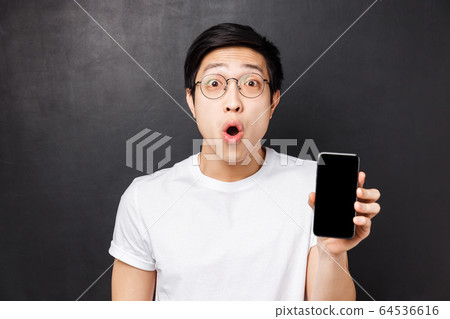 Technology, messaging and people concept. Close-up portrait of amazed and excited happy young asian man, showing mobile phone screen telling about fantastic cool new app, black background 64536616