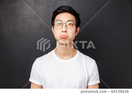 Close-up portrait of impressed asian young man in white t-shirt and glasses, look upper left corner with approval say not bad, squinting and nod acceptingly, standing black background 64536636