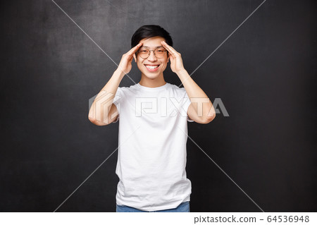 Happy charismatic young man feel well, got better after having prescribed medicine, smiling camera and hold hands near forehead as if seeing something distance, found perfect spot 64536948