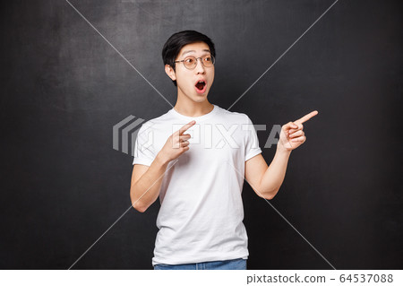 Omg wow so cool. Astonished and impressed asian guy, fan of music band seeing them live, drop jaw and gasping from amazement and happiness, pointing fingers right spot something awesome 64537088