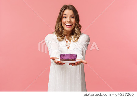 Holidays, spring and party concept. Tender, romantic and cute blond girlfriend prepared delicious dessert, asking you try it, giving person piece cake and smiling lovely, pink background 64537260