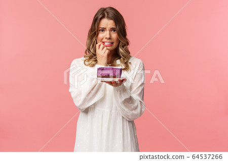 Holidays, spring and party concept. Alarmed, worried young blond girl hesitating eat cake or not, being on diet, trying stay healthy, holding dessert, biting finger nervously, pink background 64537266