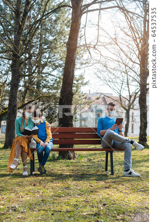 People sitting on park bench in the sun practicing social distancing 64537535
