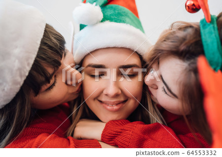 Portrait of three women friends wearing leisure clothing hugging together and kissing in cheeks 64553332