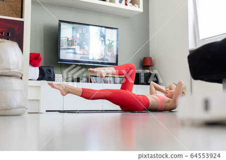 Attractive sporty woman working out at home, doing pilates exercise in front of television in her small studio appartment. Social distancing. Stay healthy and stay at home during corona virus pandemic 64553924