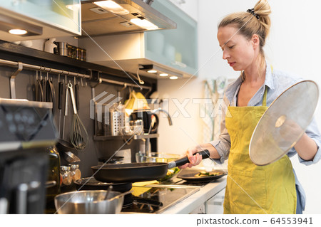 Stay at home housewife woman cooking in kitchen, stir frying dish in a saucepan, preparing food for family dinner. 64553941