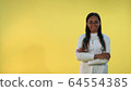 Black female doctor in lab coat smiling to the camera on yellow background. 64554385