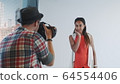 Backside view of photographer taking photo of beautiful multiracial model in studio 64554406