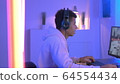 Medium shot of young black gammer in headphones playing in online shooter 64554434