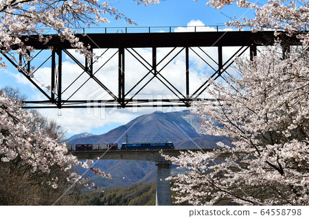 An EH-200 freight train travels over the Tachiba River Bridge in spring in Fujimi Town, Nagano Prefecture. In the foreground is the old Tachiba iron bridge (abandoned truss-type railway line). An EH-200 freight train travels over the Tachiba River Bridge in spring in Fujimi Town, Nagano Prefecture. In the foreground is the old Tachiba iron bridge (abandoned truss-type railway line). 64558798